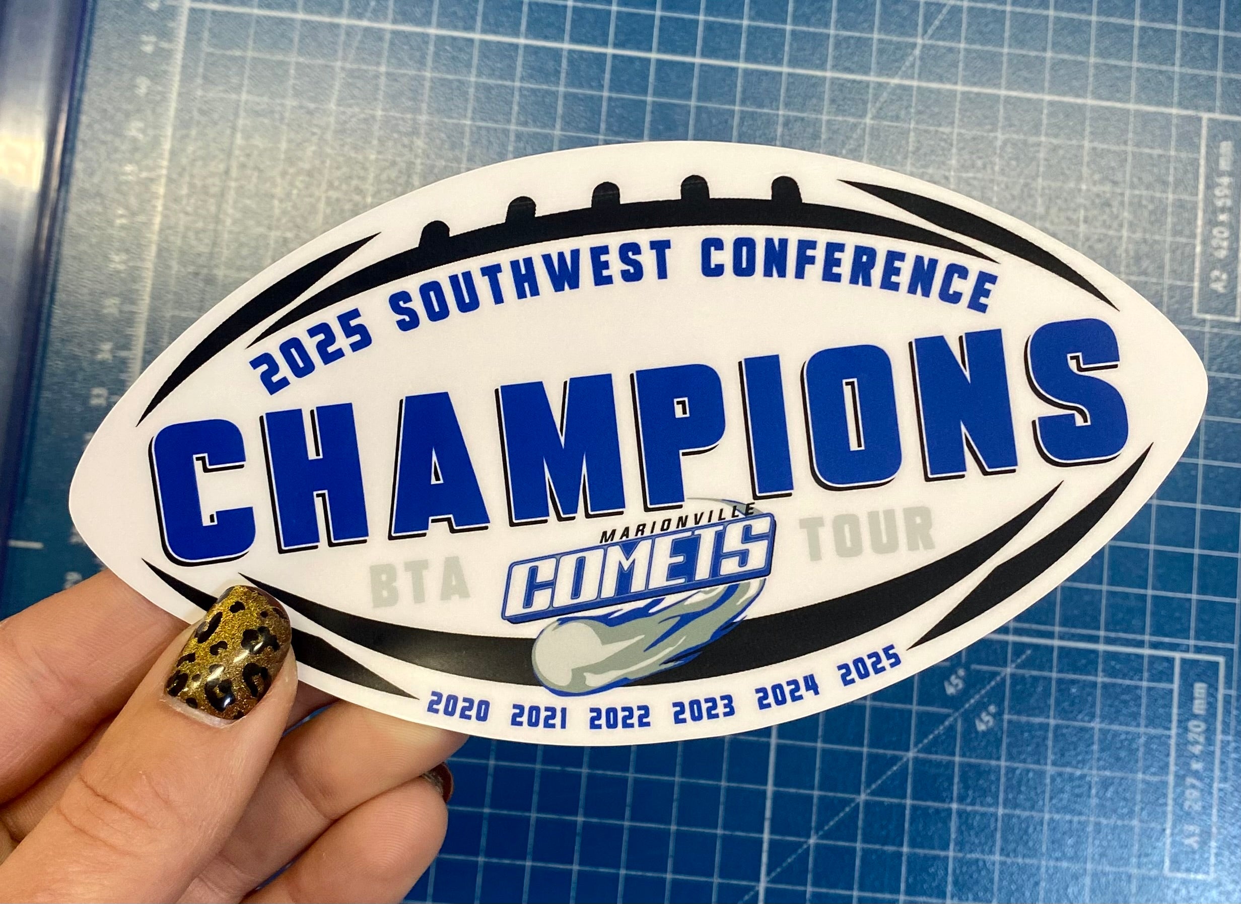 Sticker with '2025 Southwest Conference Champions' text held by a hand on a cutting mat.